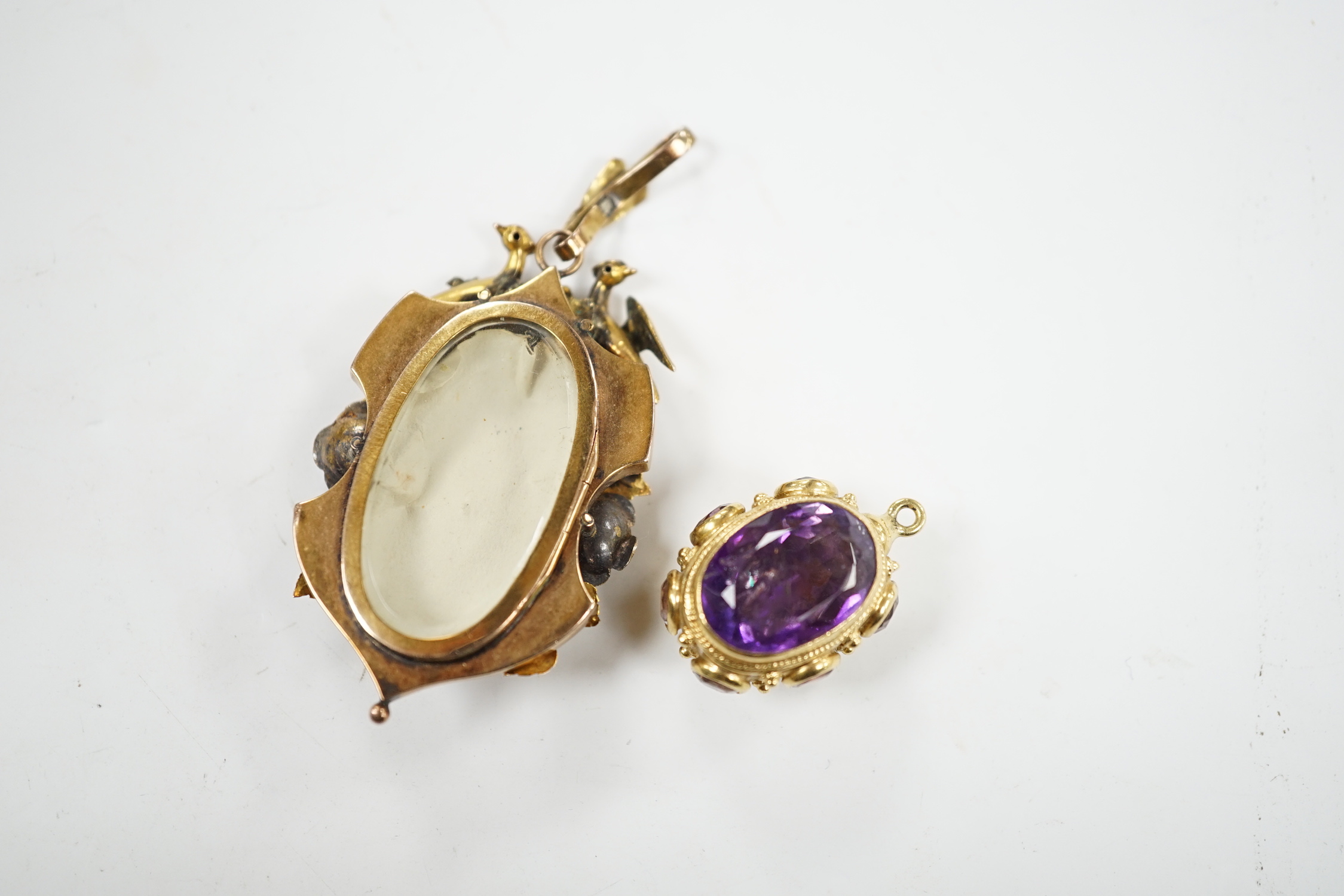 A Victorian three colour yellow metal, turquoise and seed pearl set pendant, decorated with birds and foliage, with glazed back, overall 65mm, together with a yellow metal and eight stone amethyst set charm.